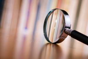 Close up of single magnifying glass with black handle, leaning on a wooden table