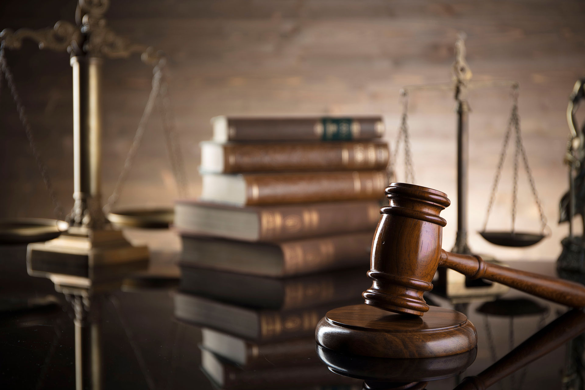 Gavel in the foreground on the right and in out of focus in the background, two scales of justice on either side and a stack of law books in the center.