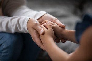 Adult hands holding a child's hand in comforting manner.